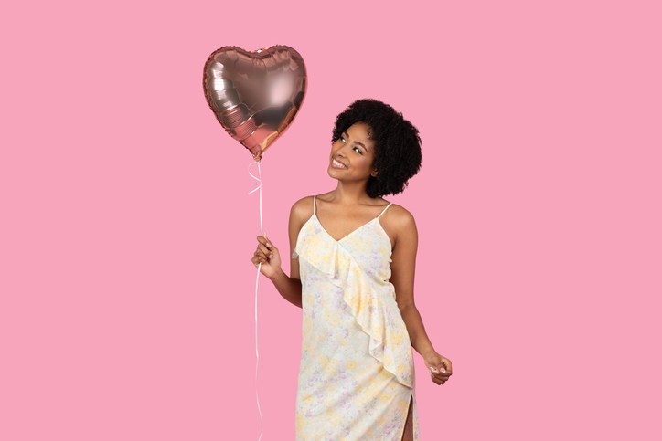 Content African American woman with curly hair, holding a heart-shaped balloon